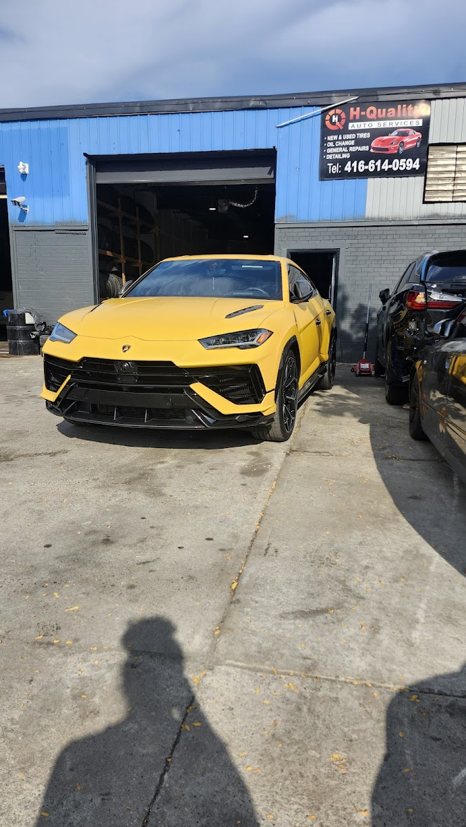 A yellow Lamborghini Urus parked outside the High Quality Auto Service bay on Iron Street.