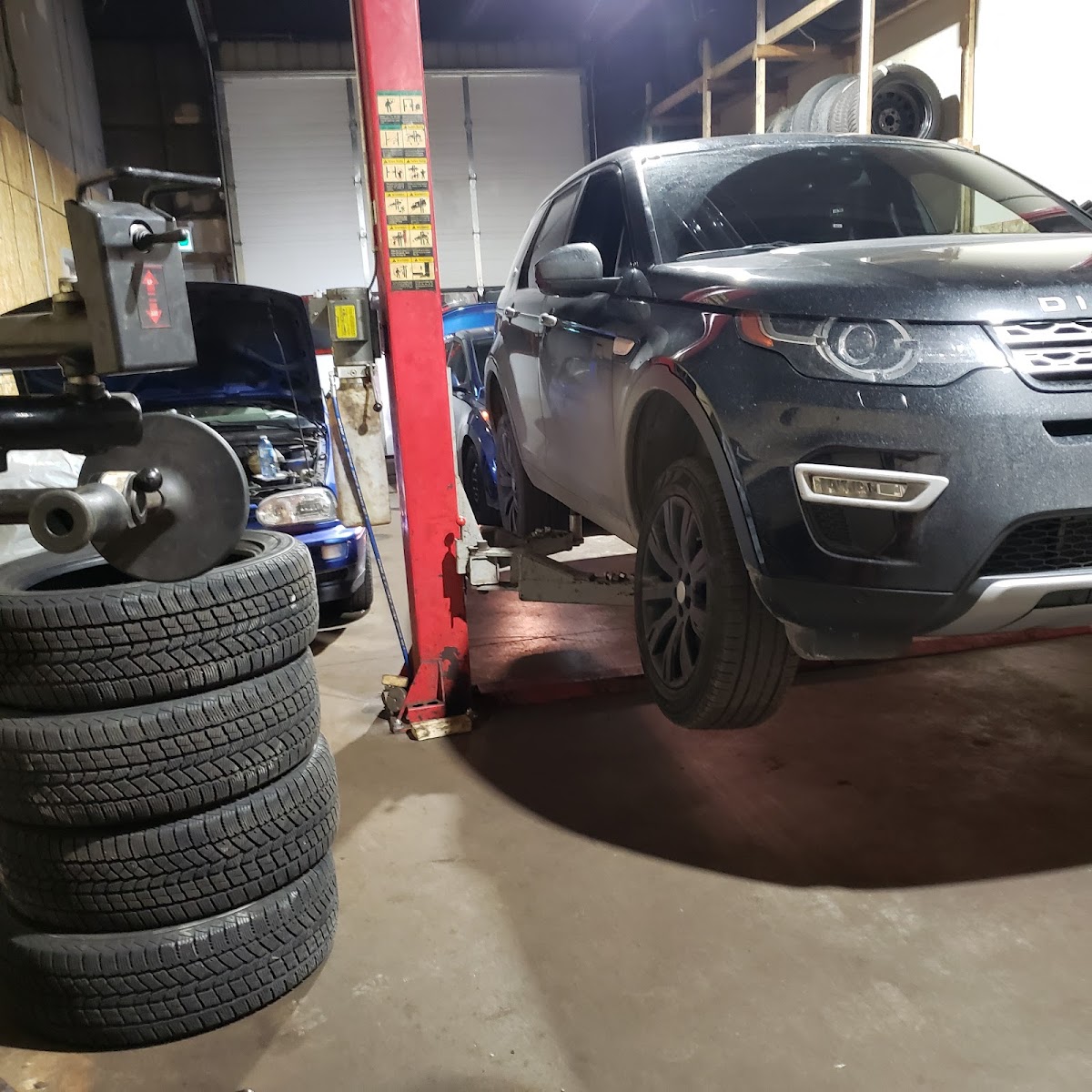 A black Land Rover lifted on a two-post hoist inside the High Quality bay, alongside a stack of winter tires.
